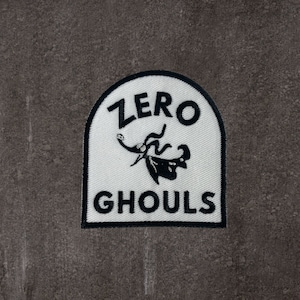 May include: White fabric patch with black stitching and a black and white illustration of a character from the movie "The Nightmare Before Christmas". The text "ZERO GHOULS" is printed in black on the patch.