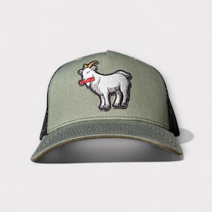 May include: A green trucker hat with a black mesh back. The hat features a white goat patch with a red tongue. The goat has gold horns and is standing on its hind legs. The hat has a curved brim.