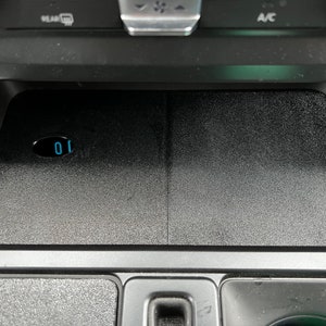 May include: A black car interior with a wireless charging pad that has a blue digital display showing the number "10".