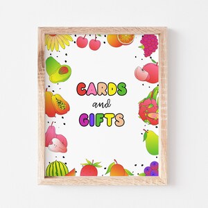 May include: A white sign with a colorful fruit border and the text "CARDS and GIFTS" in rainbow letters.