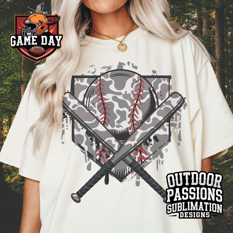 May include: A white t-shirt with a graphic of a baseball, two bats, and a home plate. The baseball and bats are camouflage patterned. The graphic has a distressed, paint-splattered look. The text "OUTDOOR PASSIONS SUBLIMATION DESIGNS" is at the bottom of the graphic.