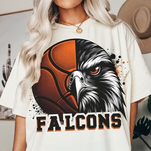 May include: White t-shirt with a graphic of a basketball and a falcon's head. The text "FALCONS" is printed below the graphic.