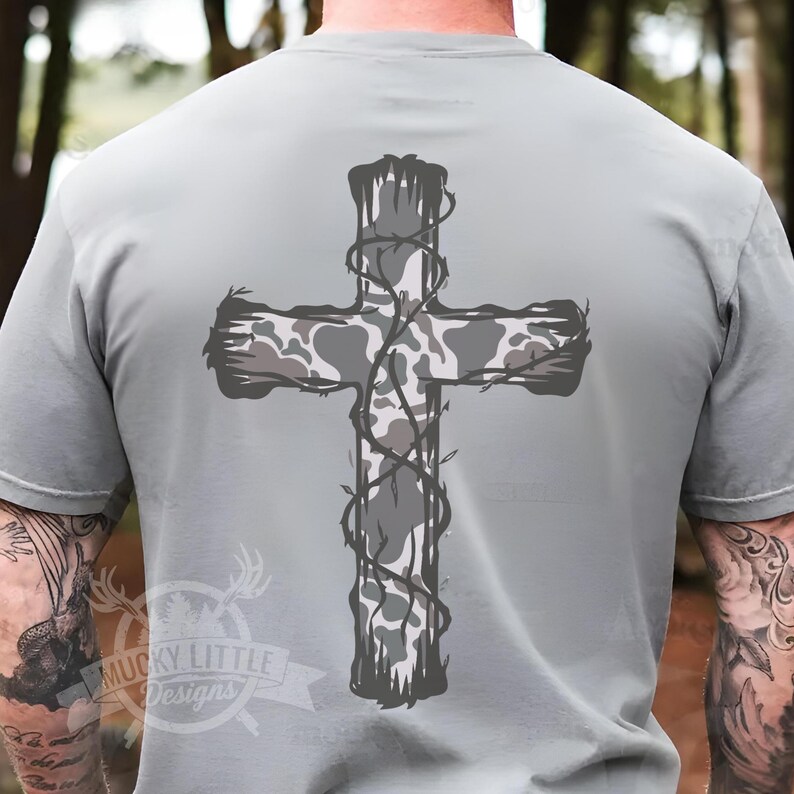 May include: A gray t-shirt with a camo cross design. The cross is surrounded by a vine pattern.