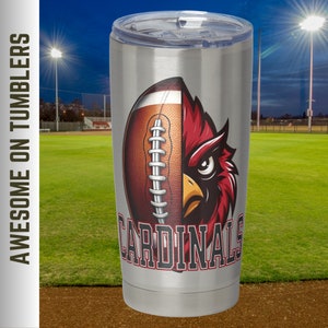 May include: A stainless steel travel mug with a football and cardinal bird design. The word "CARDINALS" is printed in red. The mug has a clear lid and is suitable for hot or cold drinks.