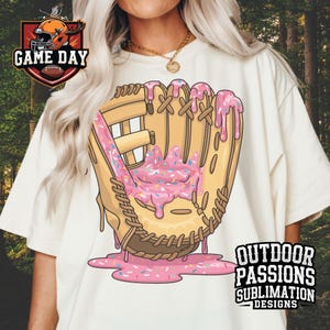 May include: A white t-shirt with a graphic of a baseball mitt covered in pink and white frosting and sprinkles. The text "OUTDOOR PASSIONS SUBLIMATION DESIGNS" is on the bottom right corner of the shirt.