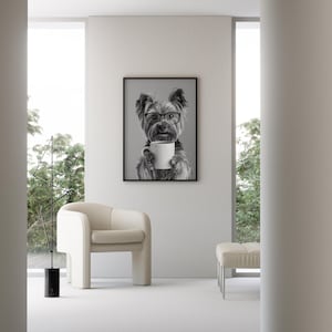 May include: A black and white photograph of a dog wearing glasses and holding a white coffee mug. The photo is framed and hanging on a white wall in a modern living room.