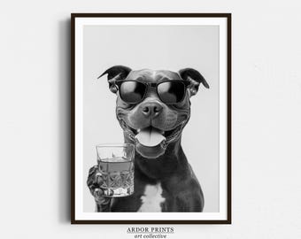 May include: A black and white photo of a dog wearing sunglasses and holding a glass of whiskey. The dog is looking at the camera and has a happy expression on its face. The photo is framed in a black frame.
