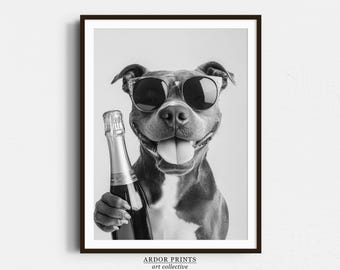 May include: A black and white photo of a dog wearing sunglasses and holding a bottle of champagne. The dog is smiling and looking at the camera. The photo is framed in a black frame with the text "ARDOR PRINTS art collective" at the bottom.