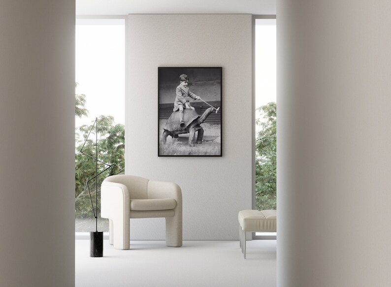K&ouml;nnte beinhalten: Ein Schwarzwei&szlig;foto eines Kindes, das auf einer gro&szlig;en Schildkr&ouml;te reitet. Das Foto ist gerahmt und h&auml;ngt an einer wei&szlig;en Wand in einem modernen Wohnzimmer.
