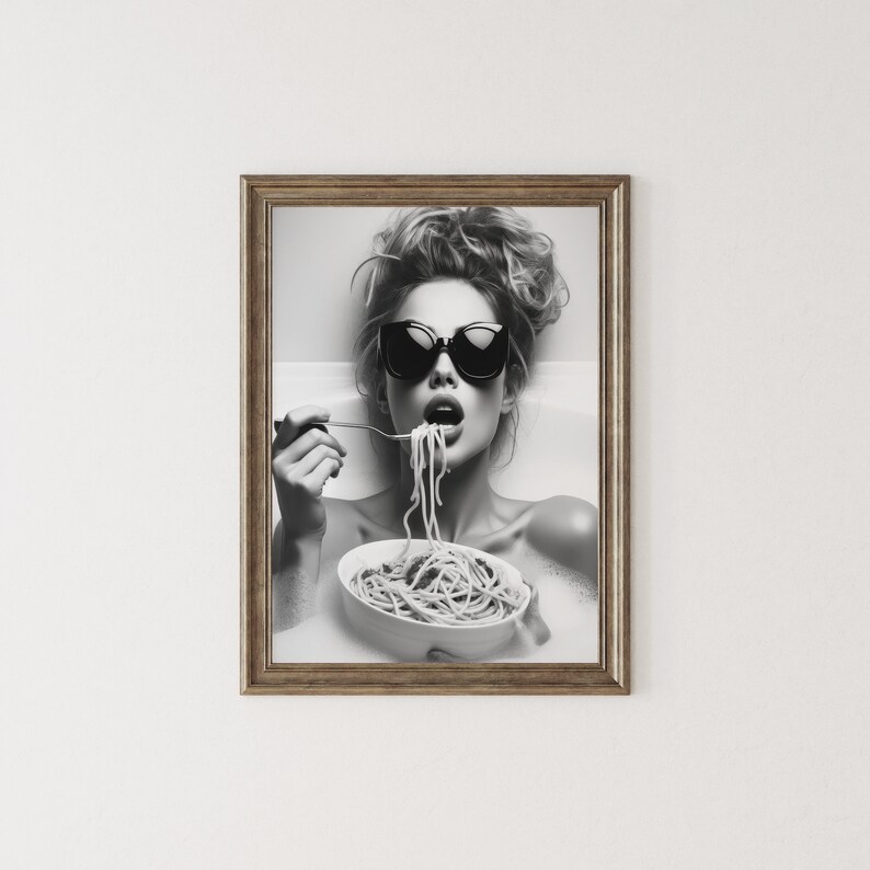 Op de afbeelding: Zwart-witfoto van een vrouw met een zonnebril die spaghetti uit een kom eet in een bad.