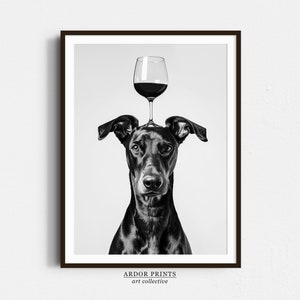 May include: Black and white photograph of a dog with a glass of red wine balanced on its head. The dog is looking directly at the camera. The image is titled "ARDOR PRINTS art collective".