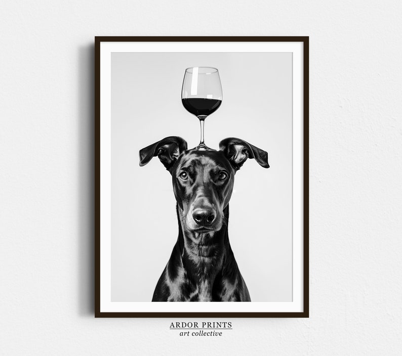 May include: Black and white photograph of a dog with a glass of red wine balanced on its head. The dog is looking directly at the camera. The image is titled "ARDOR PRINTS art collective".