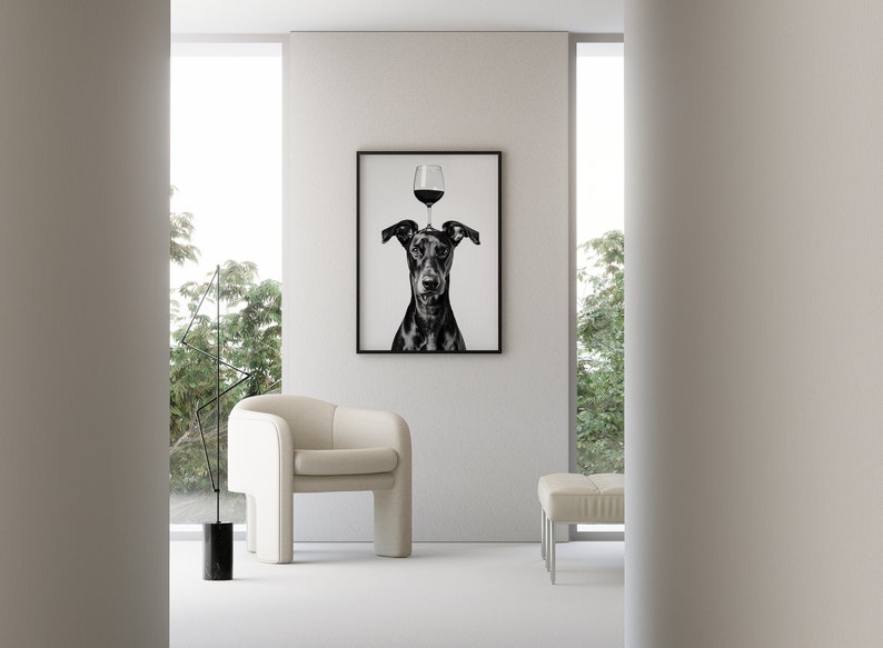 May include: Black and white photograph of a dog with a glass of red wine balanced on its head. The photo is framed and hanging on a white wall in a modern living room.