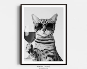 May include: A black and white photo of a cat wearing sunglasses and holding a glass of red wine. The cat is looking at the camera with a serious expression. The photo is framed in a black frame with the text "ARDOR PRINTS art collective" at the bottom.