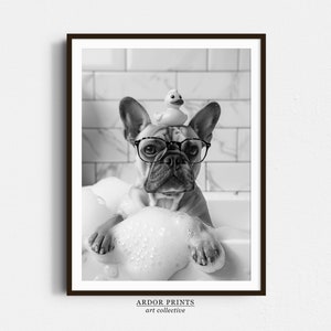 Op de afbeelding: Een zwart-witfoto van een Franse bulldog die een bril draagt en een rubberen eendje op zijn kop heeft. De hond zit in een bad vol met bubbels.