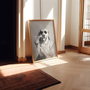Op de afbeelding: Een ingelijste zwart-witfoto van een golden retriever die een zonnebril draagt en een martini-glas vasthoudt. De hond kijkt recht in de camera en heeft een speelse uitdrukking op zijn gezicht. De foto is ingelijst in een eenvoudige gouden lijst en hangt aan een witte muur.