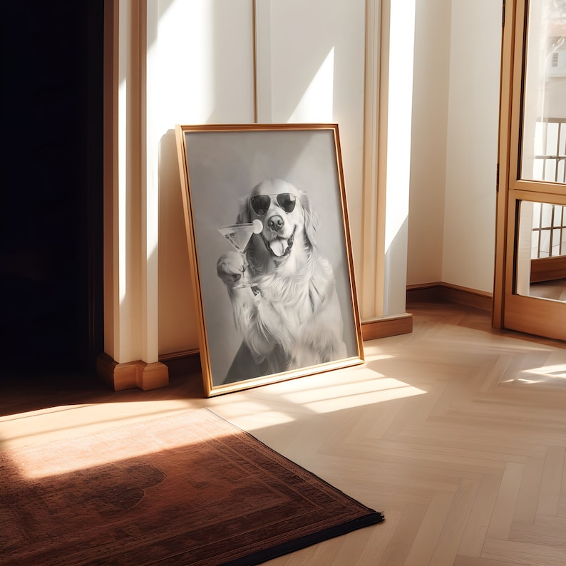 Op de afbeelding: Een ingelijste zwart-witfoto van een golden retriever die een zonnebril draagt en een martini-glas vasthoudt. De hond kijkt recht in de camera en heeft een speelse uitdrukking op zijn gezicht. De foto is ingelijst in een eenvoudige gouden lijst en hangt aan een witte muur.