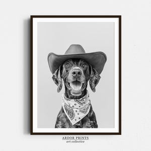 May include: A black and white photo of a dog wearing a brown cowboy hat and a bandana with a red, white, and blue pattern. The dog is looking directly at the camera and has a happy expression.