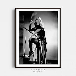 Puede incluir: Fotografía en blanco y negro de una mujer con un vestido negro y medias, de pie en una escalera y sosteniendo un cigarrillo.