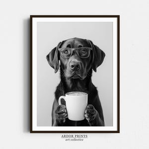 May include: Black and white photograph of a black Labrador Retriever wearing glasses and holding a white coffee mug. The dog is looking directly at the camera.