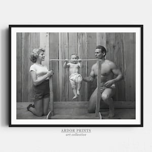 May include: A black and white photograph of a family of three. A woman in a white shirt and shorts is kneeling on the left side of the image. A man in shorts is kneeling on the right side of the image. A child is hanging from a horizontal bar in the middle of the image.