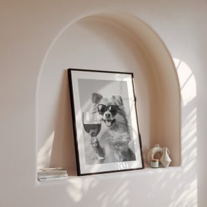 Peut inclure: Photographie en noir et blanc d'un chien portant des lunettes de soleil et tenant un verre de vin. La photo est encadr&eacute;e dans un cadre noir et accroch&eacute;e &agrave; un mur.
