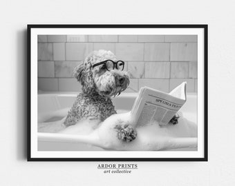 May include: A black and white photo of a dog wearing glasses and reading a newspaper while sitting in a bathtub full of bubbles.