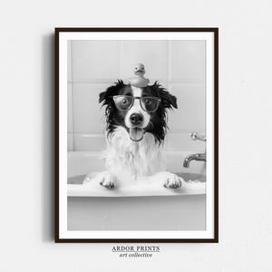 May include: A black and white photo of a dog wearing glasses and a rubber duck on its head. The dog is in a bathtub and is looking at the camera.