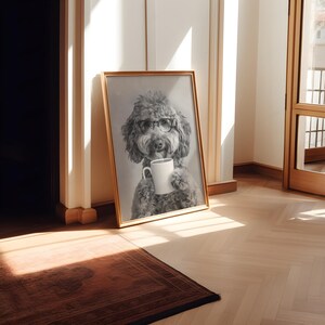 May include: A black and white photo of a dog wearing glasses and holding a white coffee mug. The photo is framed in a gold frame and is hanging on a white wall.