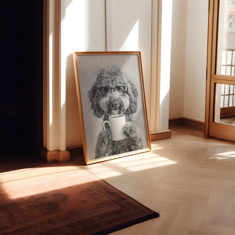 May include: A black and white photo of a dog wearing glasses and holding a white coffee mug. The photo is framed in a gold frame and is hanging on a white wall.