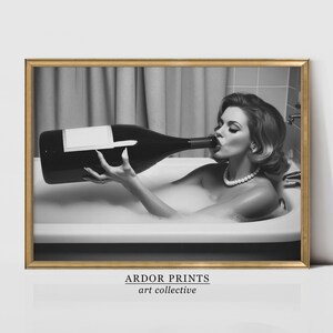 Peut inclure: Photographie en noir et blanc d'une femme dans une baignoire buvant dans une grande bouteille de vin. La femme porte un collier de perles et ses cheveux sont coiff&eacute;s en un chignon bouffant. L'image est encadr&eacute;e dans un cadre dor&eacute;.