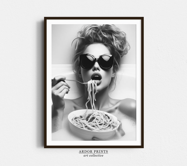 Op de afbeelding: Een zwart-witfoto van een vrouw die een zonnebril draagt en spaghetti eet in een badkuip. De vrouw kijkt naar de camera en heeft een speelse uitdrukking op haar gezicht.