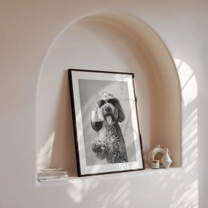 Pu&ograve; includere: Foto in bianco e nero di un cane con occhiali da sole che tiene un bicchiere di vino. La foto &egrave; incorniciata in una cornice nera e appesa a un muro.