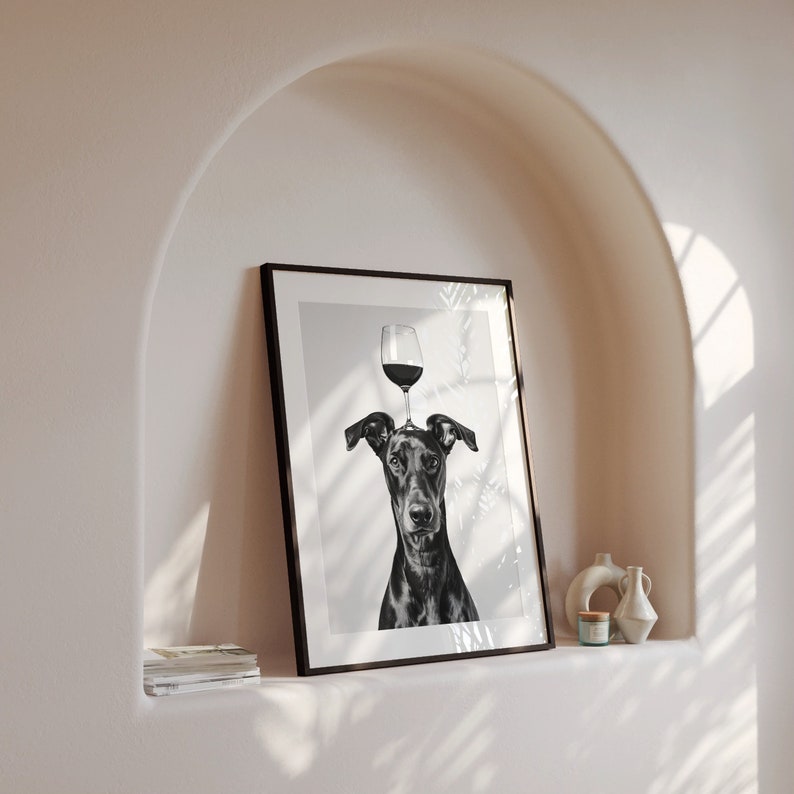 May include: Black and white illustration of a dog with a glass of wine on its head. The image is framed in a black frame and hanging on a white wall.