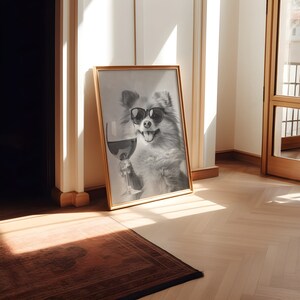 Peut inclure: Une photo en noir et blanc d'un chien portant des lunettes de soleil et tenant un verre de vin rouge. La photo est encadr&eacute;e dans un cadre dor&eacute; et est accroch&eacute;e &agrave; un mur blanc.