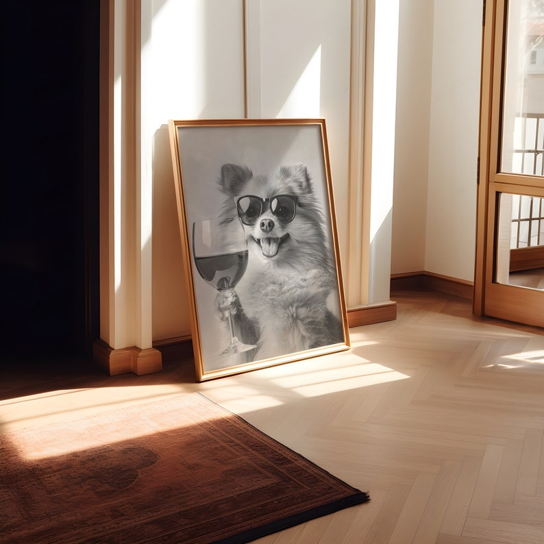 Peut inclure: Une photo en noir et blanc d'un chien portant des lunettes de soleil et tenant un verre de vin rouge. La photo est encadr&eacute;e dans un cadre dor&eacute; et est accroch&eacute;e &agrave; un mur blanc.