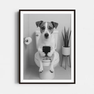 May include: A black and white photo of a dog sitting on a toilet and looking at a smartphone. The dog is wearing a collar and has a white chest and paws. The toilet is white and has a white seat. The dog is sitting on the toilet seat and holding the smartphone in its paws.