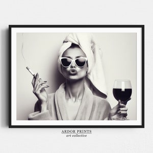 May include: Black and white photograph of a woman wearing a white towel on her head and sunglasses. She is holding a cigarette in one hand and a glass of red wine in the other. She is pouting.