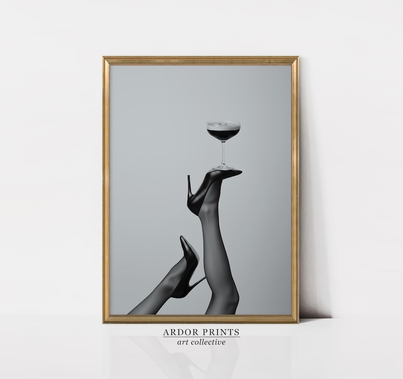 May include: Black and white framed art print featuring a pair of legs in black high heels, holding a coupe glass filled with a dark liquid. The print has a gold frame and the text "ARDOR PRINTS art collective" at the bottom.