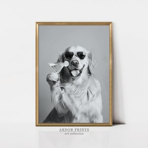 Op de afbeelding: Een zwart-witfoto van een golden retriever die een zonnebril draagt en een martini-glas vasthoudt. De hond glimlacht en kijkt naar de camera. De foto is ingelijst in een gouden lijst en heeft de tekst "ARDOR PRINTS art collective" onderaan.