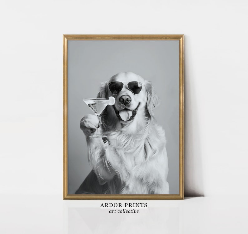 Op de afbeelding: Een zwart-witfoto van een golden retriever die een zonnebril draagt en een martini-glas vasthoudt. De hond glimlacht en kijkt naar de camera. De foto is ingelijst in een gouden lijst en heeft de tekst "ARDOR PRINTS art collective" onderaan.
