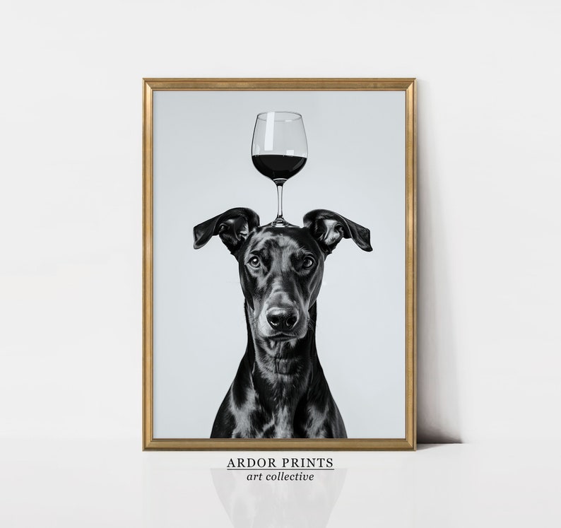 May include: Black and white photograph of a dog with a glass of red wine balanced on its head. The image is framed in a gold frame and has the text "ARDOR PRINTS art collective" at the bottom.