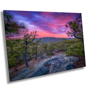 May include: A panoramic view of a rocky mountain landscape at sunset. The sky is a vibrant mix of pink, purple, and blue hues.  The foreground features large, gray rocks and a forest of evergreen trees.