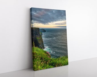 May include: A scenic view of the Cliffs of Moher in Ireland. The cliffs are tall and rugged, with green grass and wildflowers growing on the top. The ocean is a deep blue, with white waves crashing against the rocks. The sky is a mix of gray and blue, with clouds moving across the horizon.