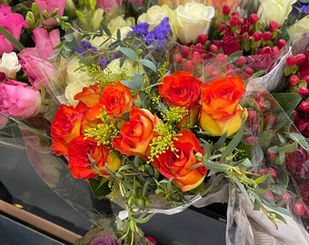 May include: A vibrant assortment of fresh-cut flowers, including roses in shades of yellow, pink, and orange. The bouquets are wrapped in clear plastic, showcasing the variety of blooms and greenery.