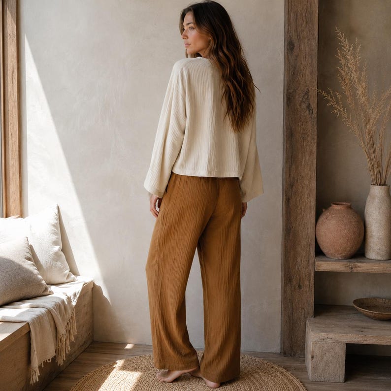 May include: A long-sleeved, cream-colored top with a ribbed texture and wide sleeves paired with loose-fitting, full-length trousers in a solid, earthy brown color. The trousers feature a straight-leg cut and a soft, textured fabric finish.