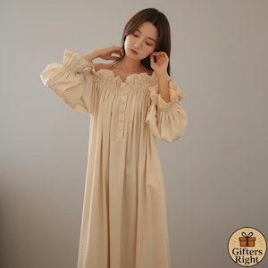 Puede incluir: Camisón largo color crema, con hombros descubiertos. Presenta un escote y mangas con volantes, con una botonadura frontal. Las mangas largas están recogidas en la muñeca. El camisón está hecho de tejido ligero.