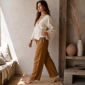 May include: A cream-colored wrap top with long, wide sleeves and a side tie closure, paired with loose-fitting, wide-leg trousers in a solid tobacco brown color. Both garments feature a subtle, vertical crinkled texture throughout the fabric.