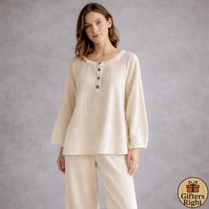 Peut inclure: Ensemble de pyjama crème. Le haut à manches longues a une encolure ronde, une patte de boutonnage et des détails froncés. Le pantalon assorti est à jambes larges. Le tissu a un aspect texturé. L'ensemble est conçu pour le confort et la détente.