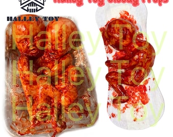 May include: Two realistic bloody baby props in a clear plastic container. One baby prop is on a white sanitary pad with red blood stains. The image includes the text "Halley Toy Bloody Props" and "Instagram: halleytoymaks".